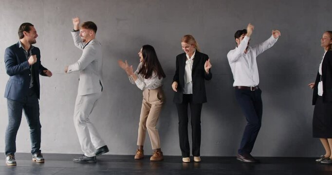 Group of happy business people having fun together, dancing against gray background. Joyful colleagues enjoying their time, celebrating success, engaging in positive team building activity in office.