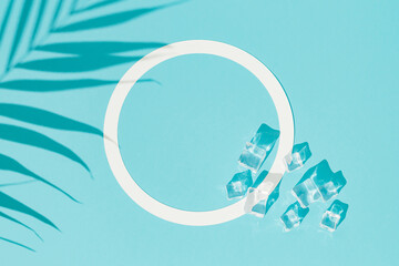 Summer day scene with ice cubes and tropical palm leaves shadow on blue background. An original...