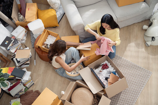 Asian girl friends unpacking stuff from cardboard boxes at the new house. Concept of people moving house, buying property and  decorating home
