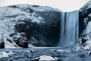 A long-exposure shot of Skógafoss waterfall in Iceland, where the rushing water transforms into a silky cascade. The contrast between frozen landscape and smooth water flow creates a surreal scene.