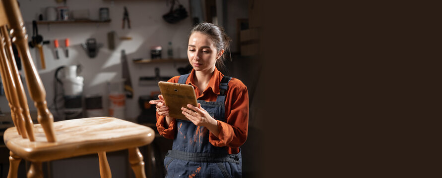 DIY and hobbies. craftsman trainee with tablet working with wooden chair in the carpentry workshop