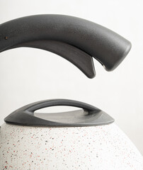 Metal teapot with white coating and black handle on light background