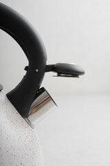 Metal teapot with white coating and black handle on light background