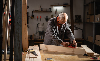 Old retired carpenter planing wooden beam working with hand tool in carpentry workshop