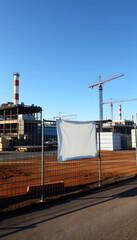 Obraz premium Blank white banner for advertisement on the fence of factory under construction. Industrial area on a sunny day, Backlit. White tone