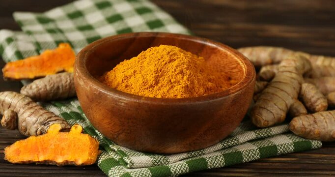Sprinkling tumeric powder into bowl at wooden table, closeup