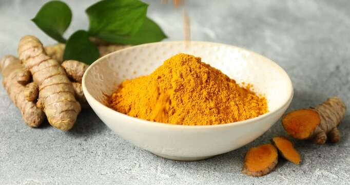 Sprinkling tumeric powder into bowl at grey table, closeup