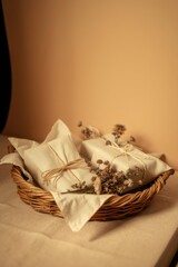 Gifts wrapped in neutral fabric and twine with dried flowers in a woven basket for a rustic aesthetic.
