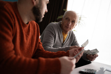Sad elderly father with adult son counting money in the living room at home. Retired man has...