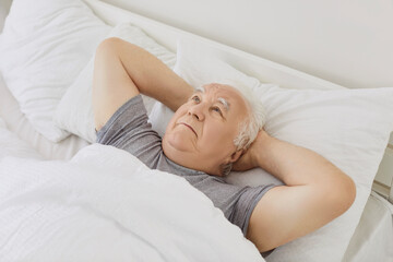 Upset senior man lies awake in cozy bed at home, dealing with insomnia and suffering from morning...