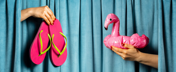 Female hands with pink flip flops and pink flamingo against blue velvet curtains. Summer concept.