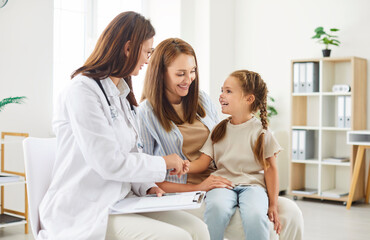 Smiling friendly woman pediatrician doctor shaking hands with a little child girl patient sitting...