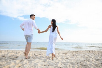 Happy couple running together on beach, back view