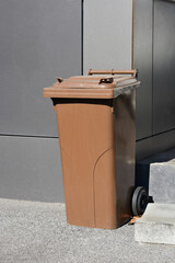 A brown compost bin for organic waste collection stands outdoors against a neutral background