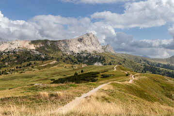 Scenic trail for hiking and mountain biking winds through autumn meadows on the Pralongia plateau in the Dolomite Alps, surrounded by rolling hills and rugged peaks