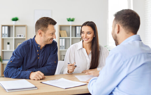Happy smiling caucasian couple signing a contract reaching agreement with a man realtor or financial advisor sitting at desk on workplace. Insurance agent consulting clients in office.