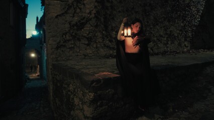Fototapeta premium Woman With Lantern Reads A Book At Night On The Streets Of The Mysterious City