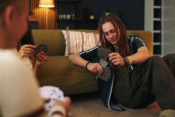 Group of friends engaging in card games while sitting on comfy floor in cozy living room setting....