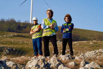 A group of engineers and environmental experts stand on a wind farm site, analyzing plans and discussing sustainable energy solutions, surrounded by wind turbines in a rural landscape