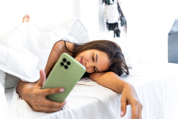 Latin woman falling asleep while using smartphone in bed: sleep hygiene issues