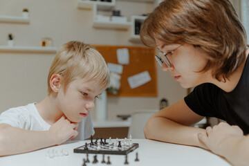 A loving mother and her son play chess together in a cozy home setting. The boy, wearing a hearing...