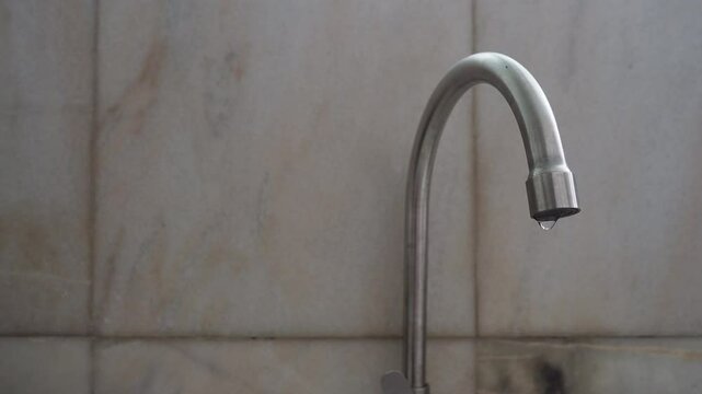 Faucet water drips - A stainless steel faucet tap with water dripping against a white marble tiles wall background