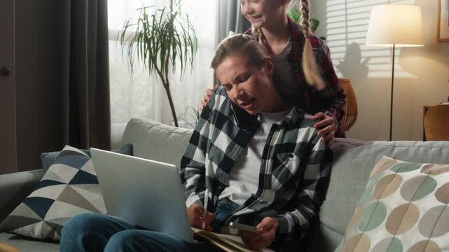 Caucasian family busy multitasking freelance working from home businesswoman mother woman female mom with laptop talking phone writing nighty noise child kid girl daughter jumping play want attention