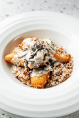 A delicious plate of crispy fried fish fillets served on a bed of buckwheat, topped with a creamy mushroom sauce, creating a hearty and flavorful dish.