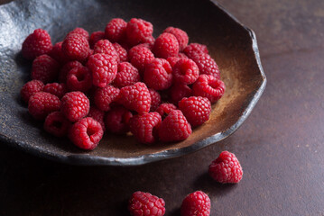 fresh raspberry in brown pottery plate on rusty background.