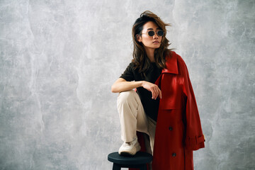 Fashionable confident woman wearing red coat and stylish casual outfit posing at studio.