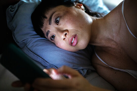 Asian stressed woman looking at smartphone in bed