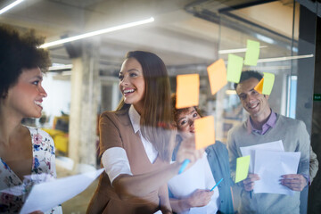 Diverse young group of people using sticky notes while working together on a project in a startup...