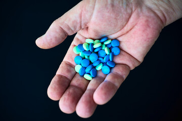 Pills of various colors on the palm of one hand. Black background. Medical devices. Close-up of pills.