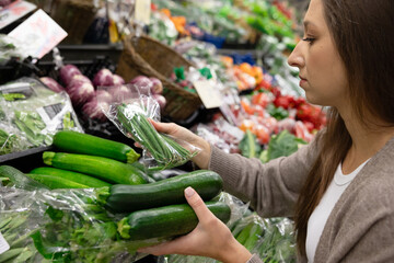 A woman compares zucchini in the produce section of a supermarket. The concept of choosing fresh vegetables, choosing healthy food and making conscious food choices