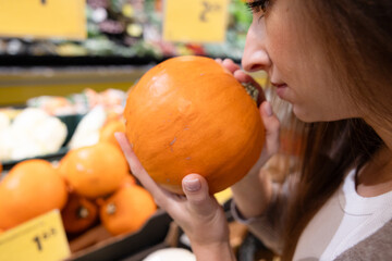 Fototapeta premium Woman smelling a fresh pumpkin in a supermarket. Concept of choosing high-quality ingredients, freshness, and mindful food shopping for a healthy lifestyle