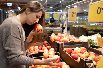 Woman smelling a fresh apple in a supermarket. Concept of choosing high-quality ingredients, freshness, and mindful food shopping for a healthy lifestyle