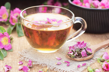 Dog rose floral  tea in a glass cup with fresh and dry flowers on wooden background, closeup, spring floral drink, natural medicine and naturopathy concept