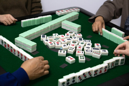 Four players are engrossed in a strategic mahjong game around a green electric mahjong table, hands ready