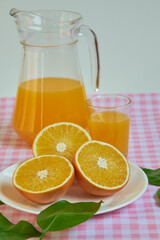 Freshly squeezed orange juice, refreshing and healthy, on a table with a pink and white checkered tablecloth, decorated with green leaves.