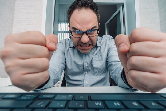 businessman in a shirt in the office punches the keyboard. angry man swearing and cursing against information technology and his compuiter worries and hassles - concept of hating computers