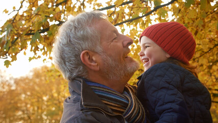 Close Up Of Loving Grandfather Cuddling Granddaughter On Autumn Walk Through Countryside