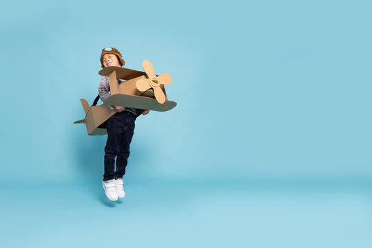 Asian little boy aviator playing and jumping with cardboard airplane isolated on blue sky background, Kid toy diy concept