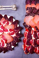 Sliced meat on a plate and tongs on a gray background