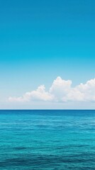 Obraz premium A serene seascape featuring clear turquoise waters under a bright blue sky with soft, white clouds in the distance.
