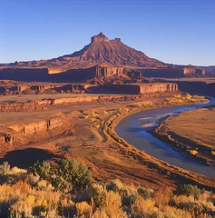 Gordijnen River meanders through a desert landscape illuminated by the warm light of dawn or dusk towards a prominent mesa. © watz