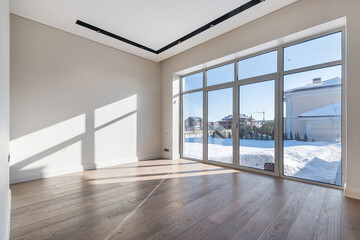 A spacious empty room in a luxurious mansion.  Unfurnished. Panoramic window with a view of the winter landscape on a sunny day.
