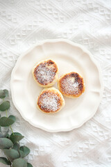 On an elegant and beautiful plate, there are three baked cheesecake that are generously topped with coconut on white fabric.