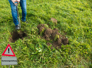 Gartenumgestaltung Schild Person mit Schaufel auf Wiese gr&auml;bt Loch
