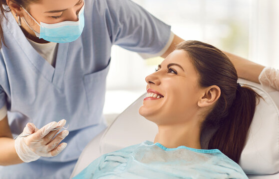 Cheerful nurse or doctor orthodontist conducting an oral checkup on a happy female patient using dental instruments in the clinic. Comprehensive dental care provided by the dentist.