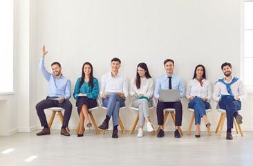 Job candidates sitting on modern office chairs in row, business people waiting for job interview,...